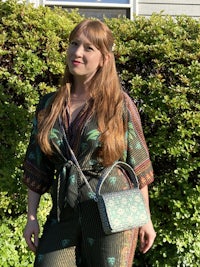 a woman in a green jumpsuit standing in front of bushes