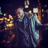a man in a leather jacket is laughing on the street at night