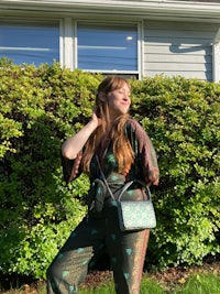 a woman in a green jumpsuit posing in front of bushes